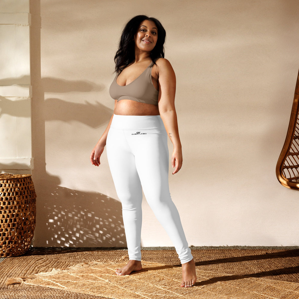 Woman wearing white high-waisted Overtuned Yoga Leggings made from stretchy polyester and spandex, posing in a bright room