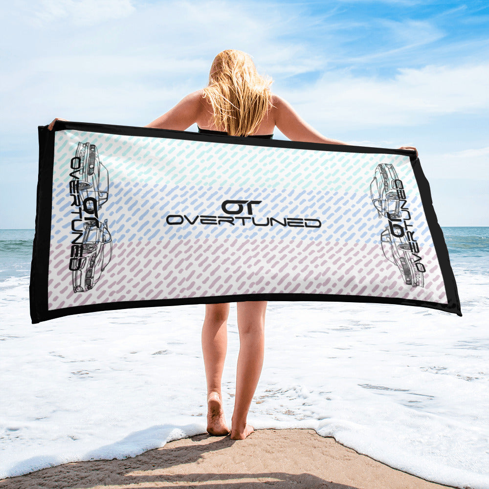 Person holding a vibrant look towel with Overtuned logo by the ocean on a sunny day